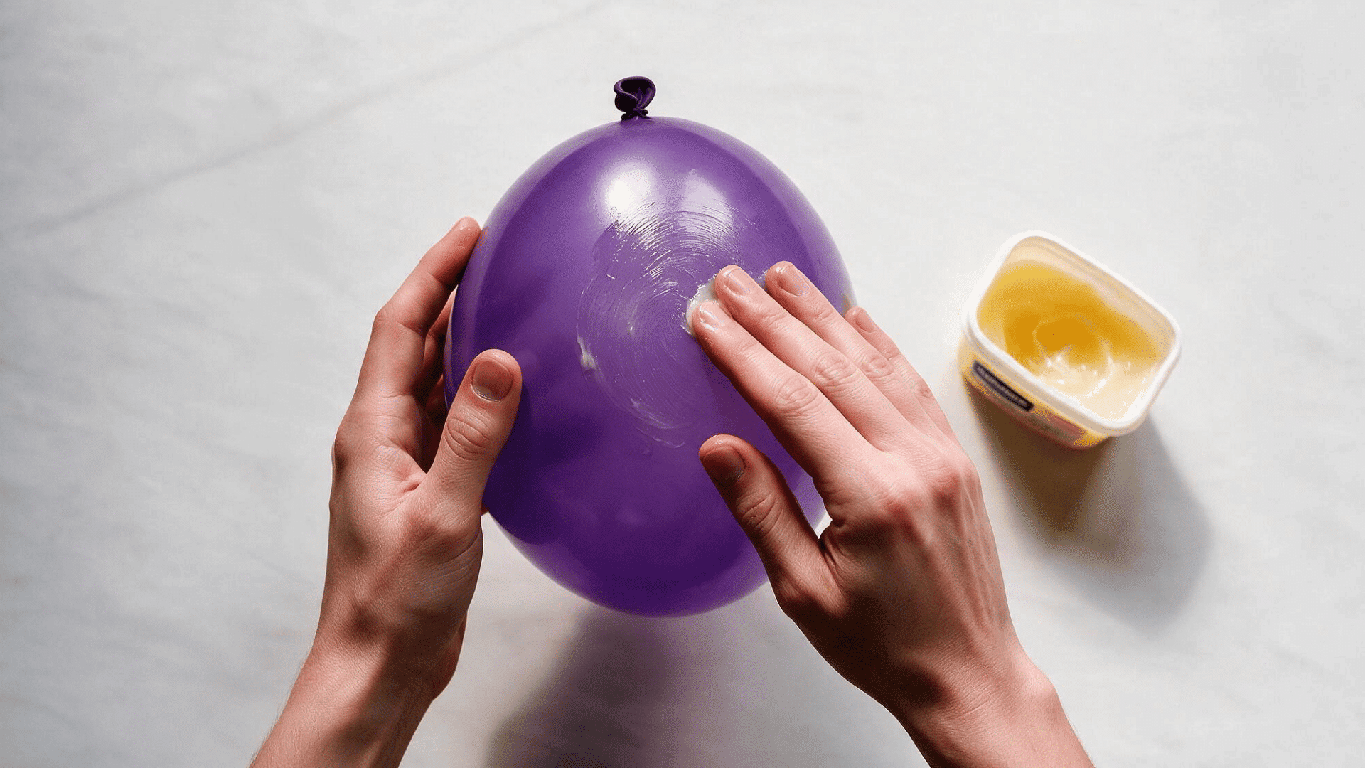hands rubbing petroleum jelly onto a green balloon to prepare it as a paper mache form