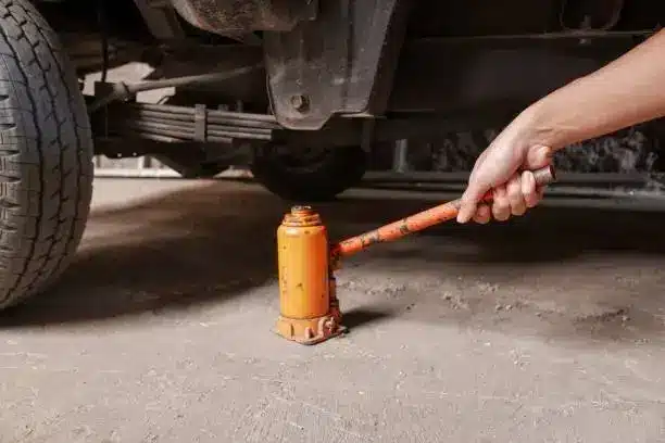 Car being lifted with an orange hydraulic jack in a garage setting