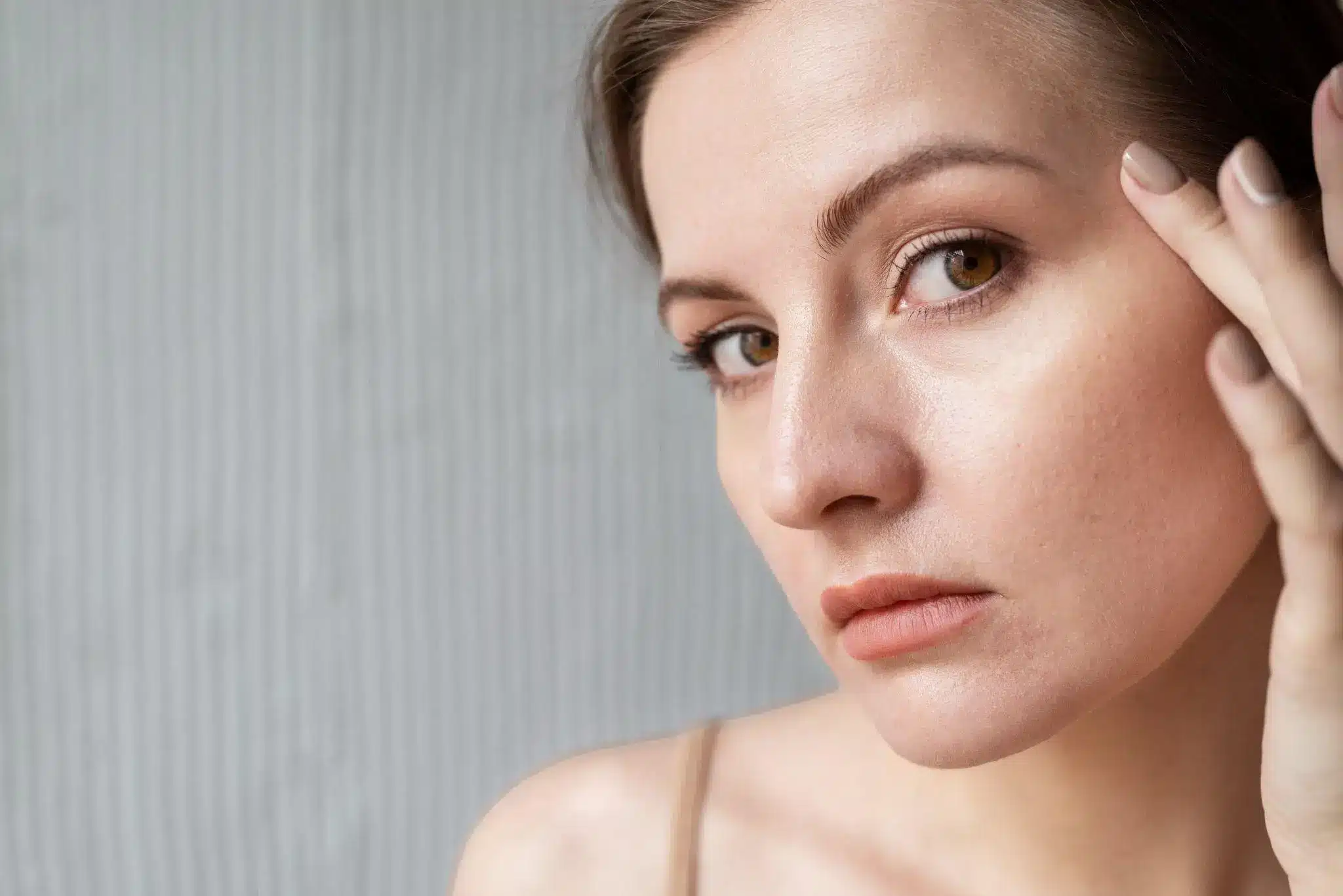 Close-up of a woman's face with a neutral expression, hand touching temple