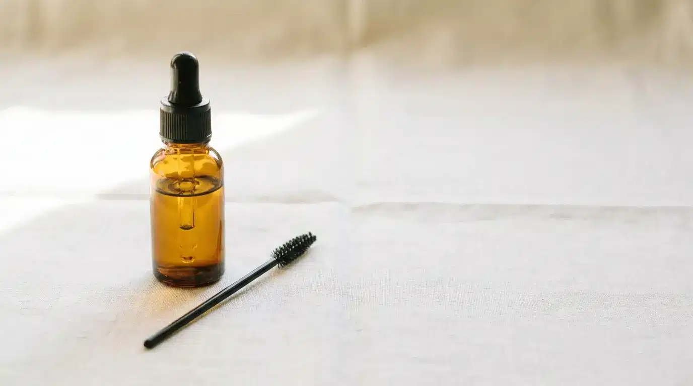 Amber dropper bottle and mascara brush on white fabric in soft natural light