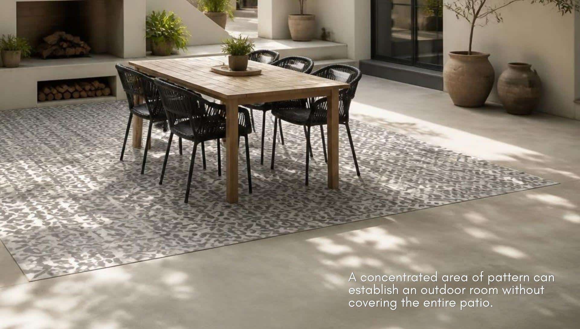Wooden outdoor dining table with black wicker chairs on patterned rug in bright courtyard patio