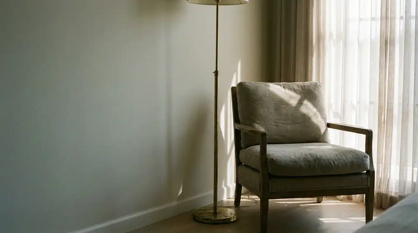Armchair by a sheer-curtained window with a floor lamp, warm afternoon light filling a quiet reading corner